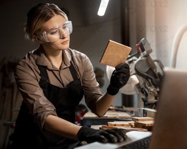 Female carpenter with safety glasses looking piece wood studio