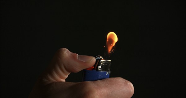 Lighter in Hand with Flame against Black background