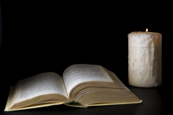 Open book illuminated by candlelight isolated on a black background