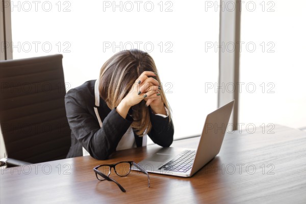 Young female manager taked of glasses after typing on netbook keyboard while sitting at table and