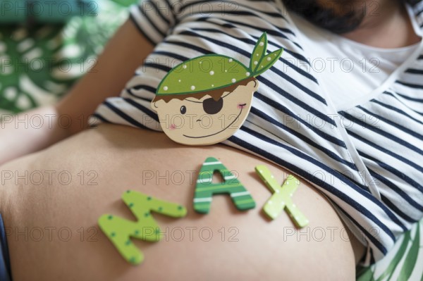 A wooden replica of a baby boy's face and letters for the name Max lie on a pregnant woman's belly