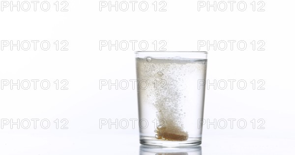 Tablets Falling and Dissolving into a Glass of Water against White Background