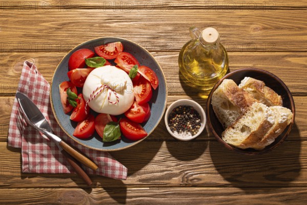 Italian salad with fresh tomatoes, burrata cheese, basil served on ceramic plate with ciabatta