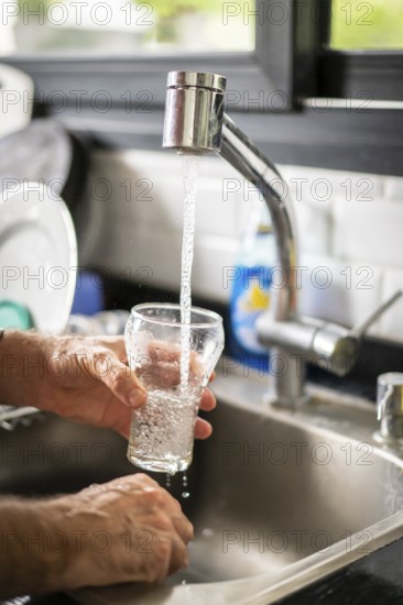 Man pouring water into glass in kitchen, closeup
