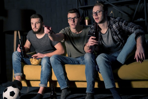 Front view male friends watching sports tv together while having snacks beer