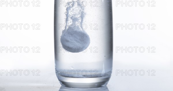 Tablets Falling and Dissolving into a Glass of Water against White Background