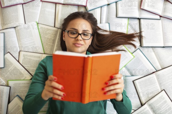 Top view of female student lying on books and reading during exam preparation