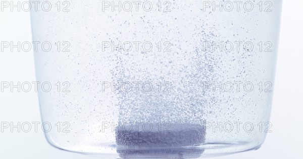Tablets Falling and Dissolving into a Glass of Water against White Background