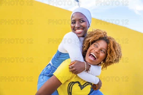 Happy scene of a muslim woman piggybacking an african friend outdoors