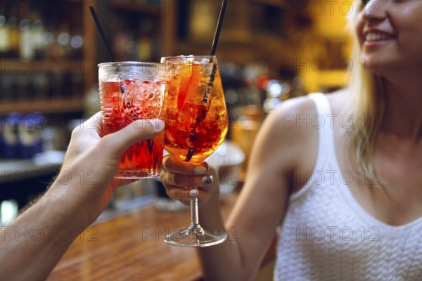 Woman and man raising a glasses of coktails in the bar background