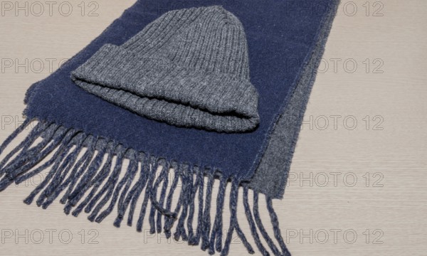 Gray knit cap laying on blue scarf on wood grain background, South Korea, South Korea, Asia