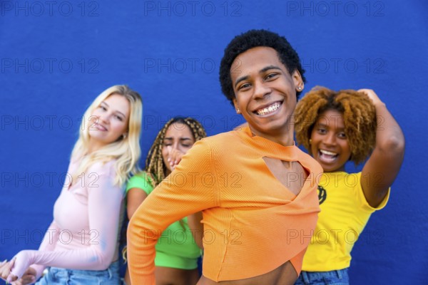 Close-up of a transgender person dancing happily with multi-ethnic friends next to a blue wall