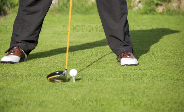 Golfer addresses golf ball with driver in tee box