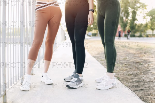 Cropped photo of three pairs of female legs of young girls in sport leggings and sneakers outdoors,