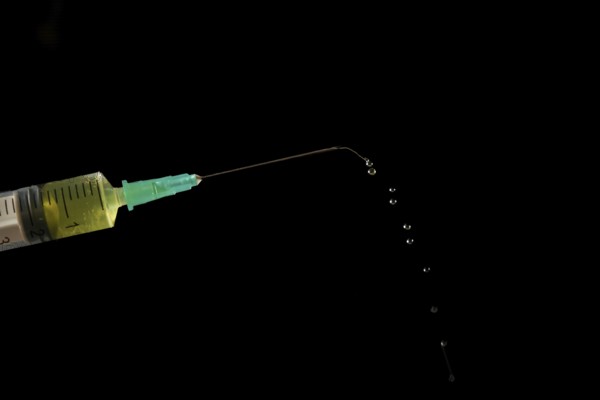Syringe with needle, a row of drops of yellow liquid coming out, isolated on black background and