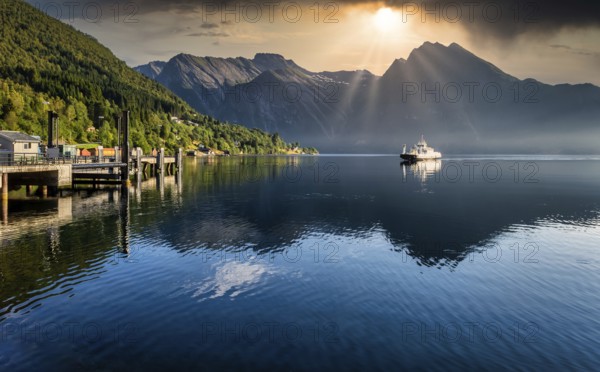 Ferry arriving on fjord during sunrise in norway with mountains in background