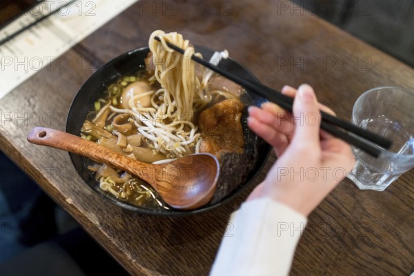 Woman using chopsticks to eat a ramen soup served on a bowl in a restaurant
