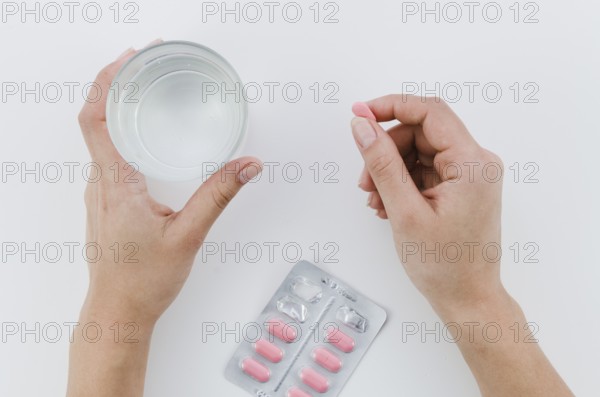 Close up woman s hand holding pink pills glass water white background