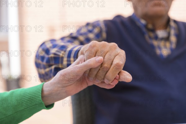 Detail of the hands of two elderly people in the garden of a nursing home or retirement home