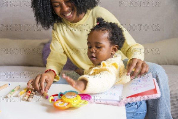 Little cute african daughter and mother playing in the sofa with toys and books