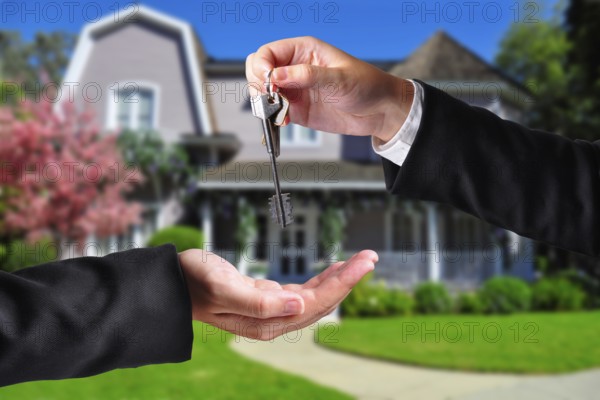 A hand giving a key to another hand. Both persons in suits and a house in the background