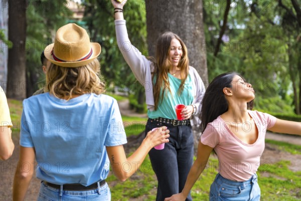 Multiethnic group of birthday party in the city park having fun and dancing with colored cups