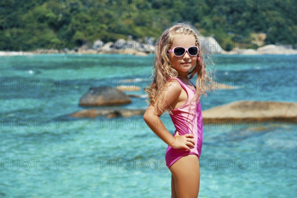 Cute little girl in sun glasses posing on beautiful tropical beach. Summer, fun and vacations