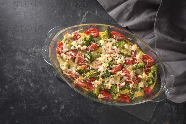 Casserole from broccoli, tomatoes, onions, feta and cheese, healthy vegetable dish on a dark gray