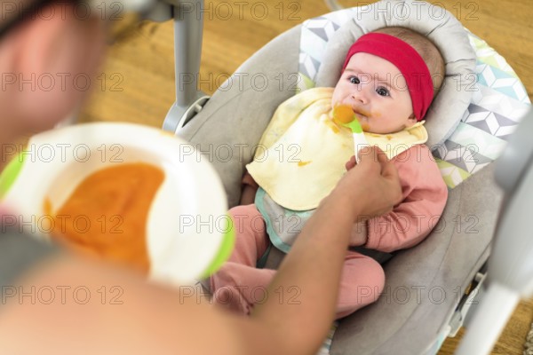 Mother feeding hungry five month old funny baby with solid food. Beagle dog watching curiously