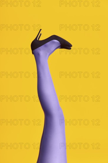 Raised females legs in bright tights and stylish high heels shoes on yellow background. Relax,