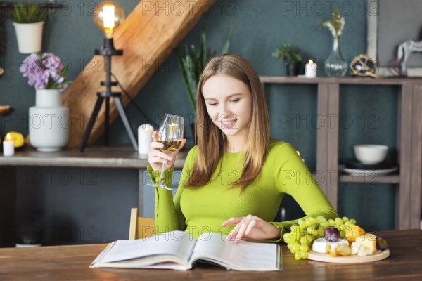 Young woman reading an interesting magazine at wooden table with fruits and wine on a weekend at
