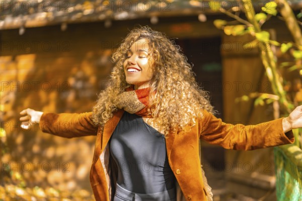 Woman with curly hair inhaling and closing eyes outdoors in a park in autumn