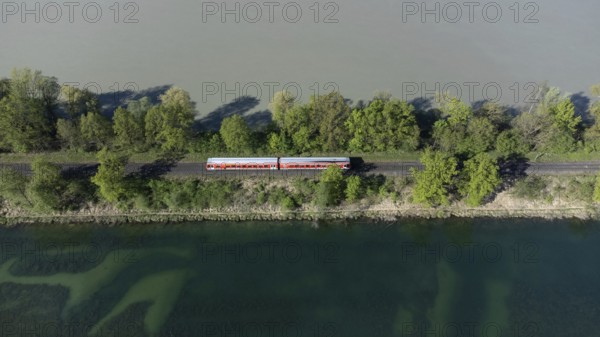 A red local railway runs on an embankment between two bodies of water with different colours, drone