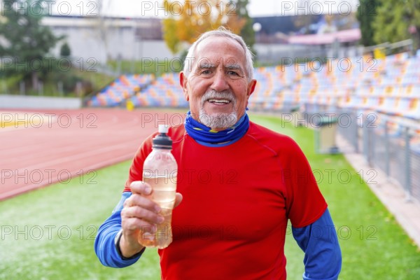 Proud old man with a reusable bottle of water after exercising in a track and field