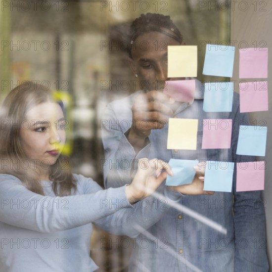 Front view man woman putting sticky notes office window