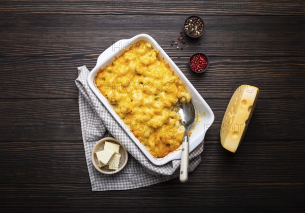 Close-up of baked mac and cheese in white casserole on rustic wooden background, with seasonings,