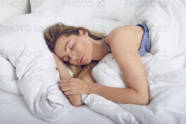 Woman sleeping in bed under white quilt with head on pillow