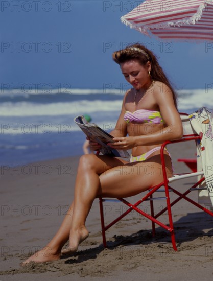 Young woman reading newspaper on beach, journal