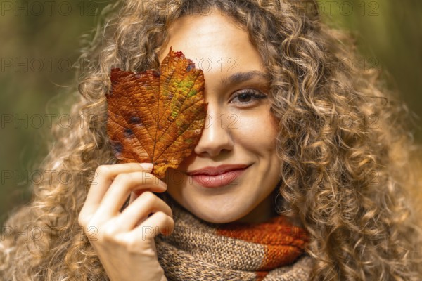 Close-up portrait of a beauty woman hiding one eye with a fallen leaf
