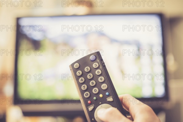 TV remote control in the foreground, tv in the blurry background. Film night with vod streaming