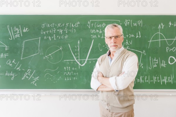 Elder professor standing near chalkboard classroom