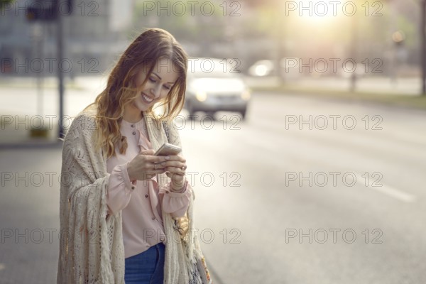 Attractive young woman checking a message on her mobile phone with a happy smile as she stands at