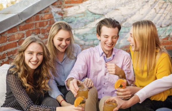 Group of young happy people friends drinking fruit cocktails together on house terrace, smiling and