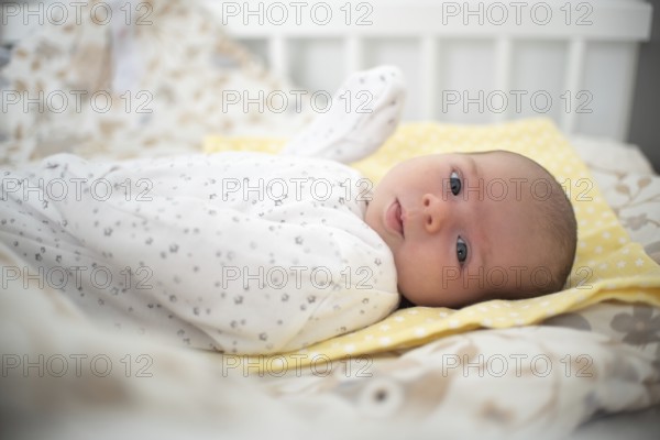 Newborn baby is lying on its side in baby crib in bright room