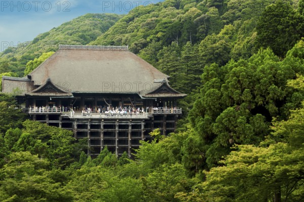 Distant view of Kiyomizu-dera temple nestled in green forest crowded with throngs of tourist