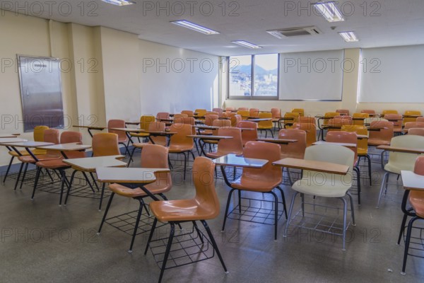 Classroom with empty desks arranged haphazardly with lights turned on and sunshine coming through