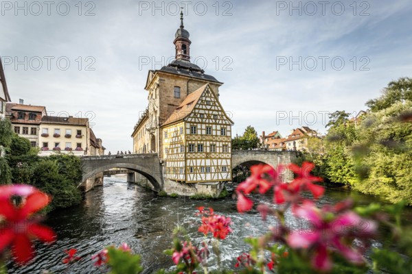 Colourful half-timbered house on a bridge with foreground of bright flowers over a river, old town