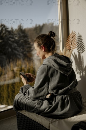 Woman in bathrobe sitting with mobile phone in a relaxation room during a wellness meal