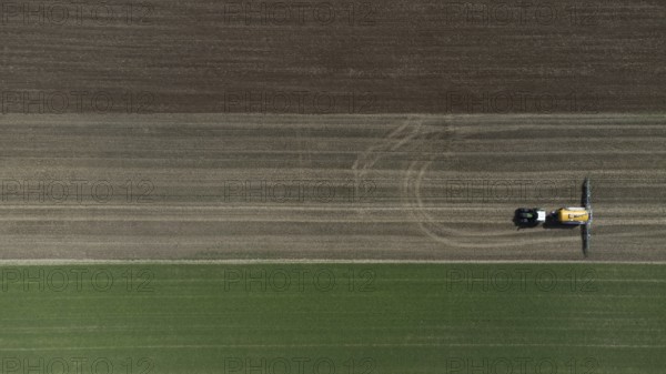 A green tractor with a yellow slurry tanker fertilises a harvested field, bird's eye view, drone