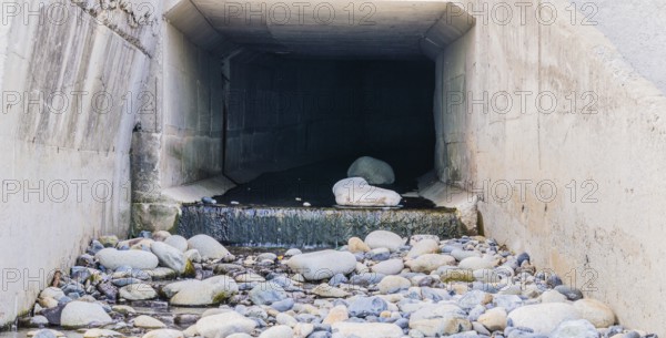 Concrete tunnel at Pebble Beach in South Korea with water running onto large rocks and stones,